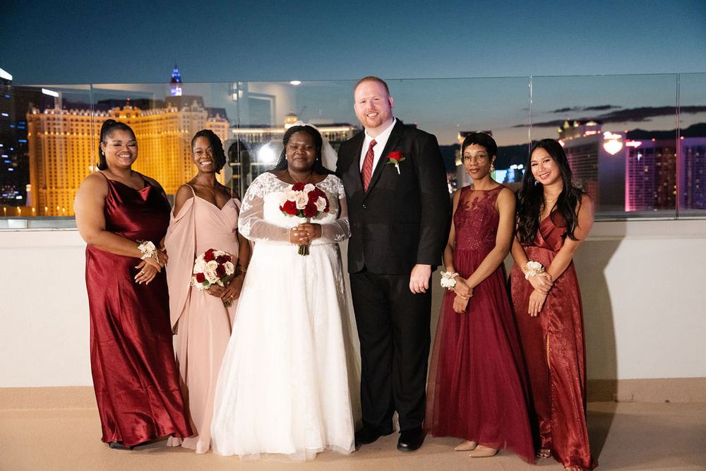 Wedding party poses on rooftop in Las Vegas, bride in white gown with bridesmaids in burgundy dresses and groom in black suit.