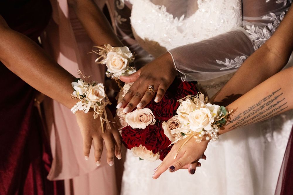 Bride and bridesmaids displaying wrist corsages and bridal bouquet with red and white roses at wedding.