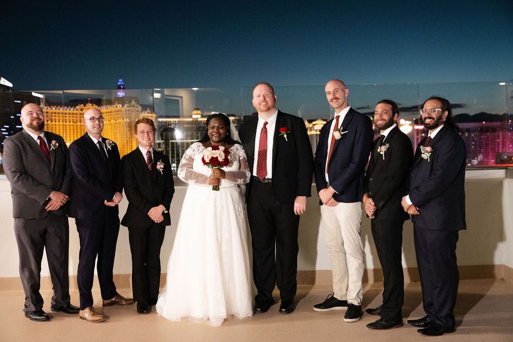 Wedding party poses on rooftop at night with Las Vegas Strip lights glowing in the background.