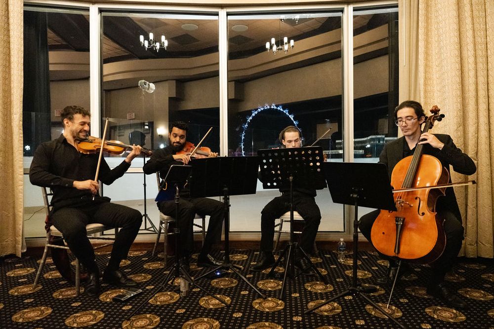String quartet performing with violins and cello in elegant venue with London Eye visible through window.