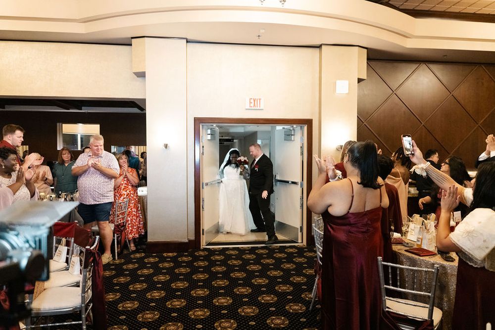 Bride and groom make grand entrance at wedding reception as guests cheer and photograph the newlyweds.