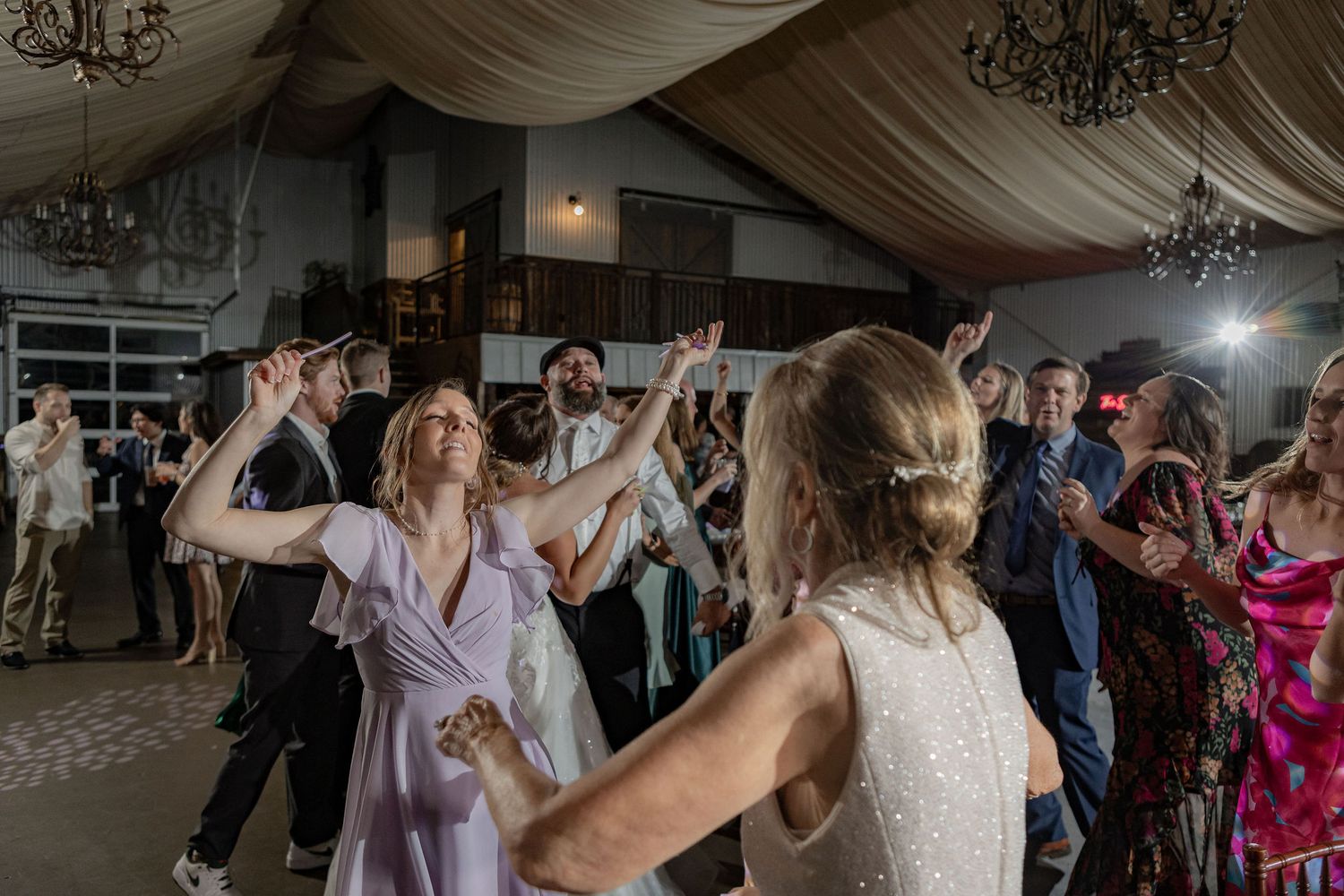 Guests dancing under the draped ceiling and chandeliers inside the Blue Barn at a Rockin' H Ranch wedding, Palm City FL
