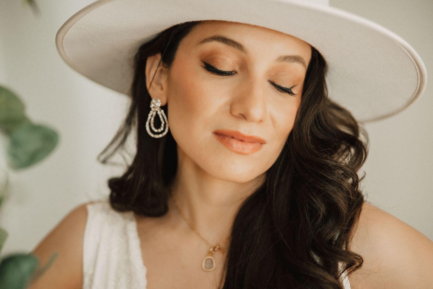 Elegant portrait with white hat, dangling earrings and soft makeup in a dreamy natural light setting.