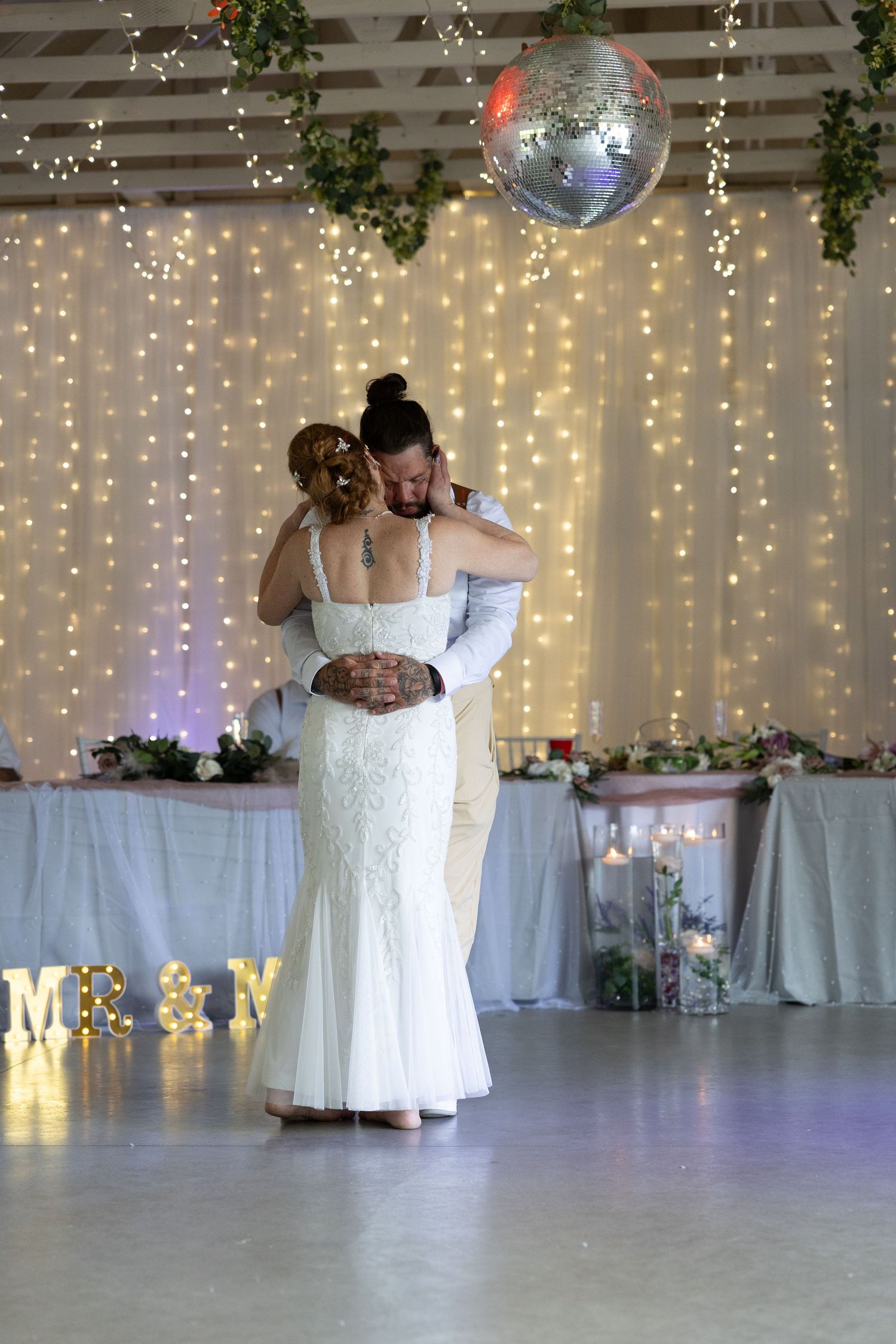 Bride and groom share their first dance under a disco ball with fairy lights backdrop at elegant wedding reception.