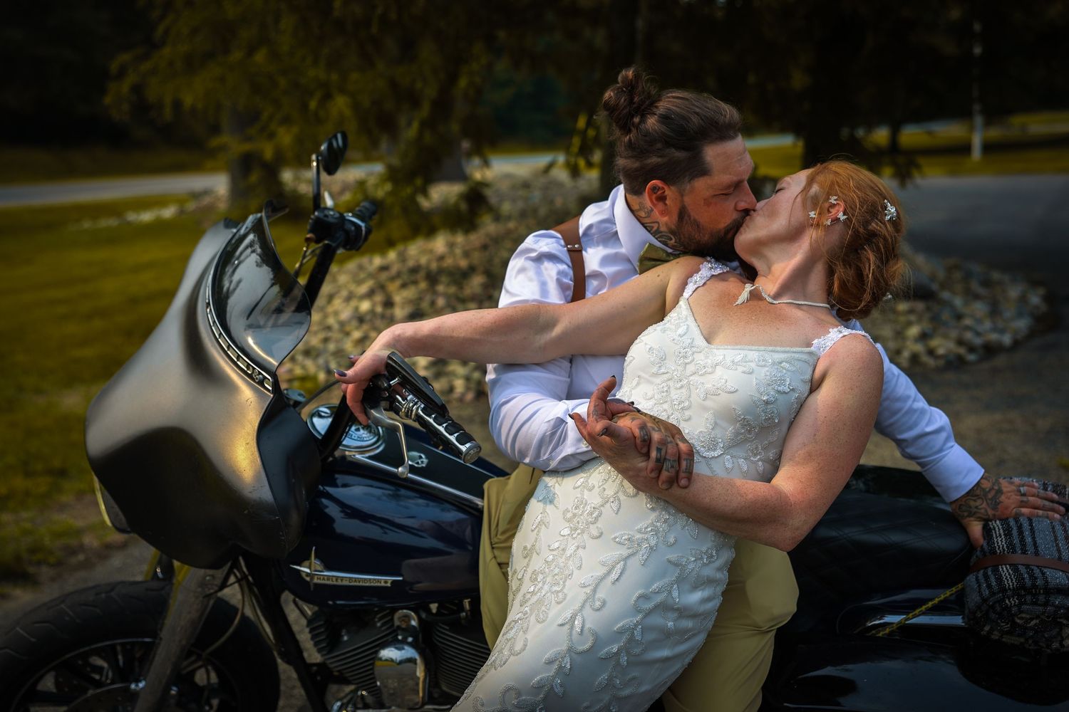 Bride and groom sharing a romantic kiss beside a motorcycle on their wedding day outdoors.