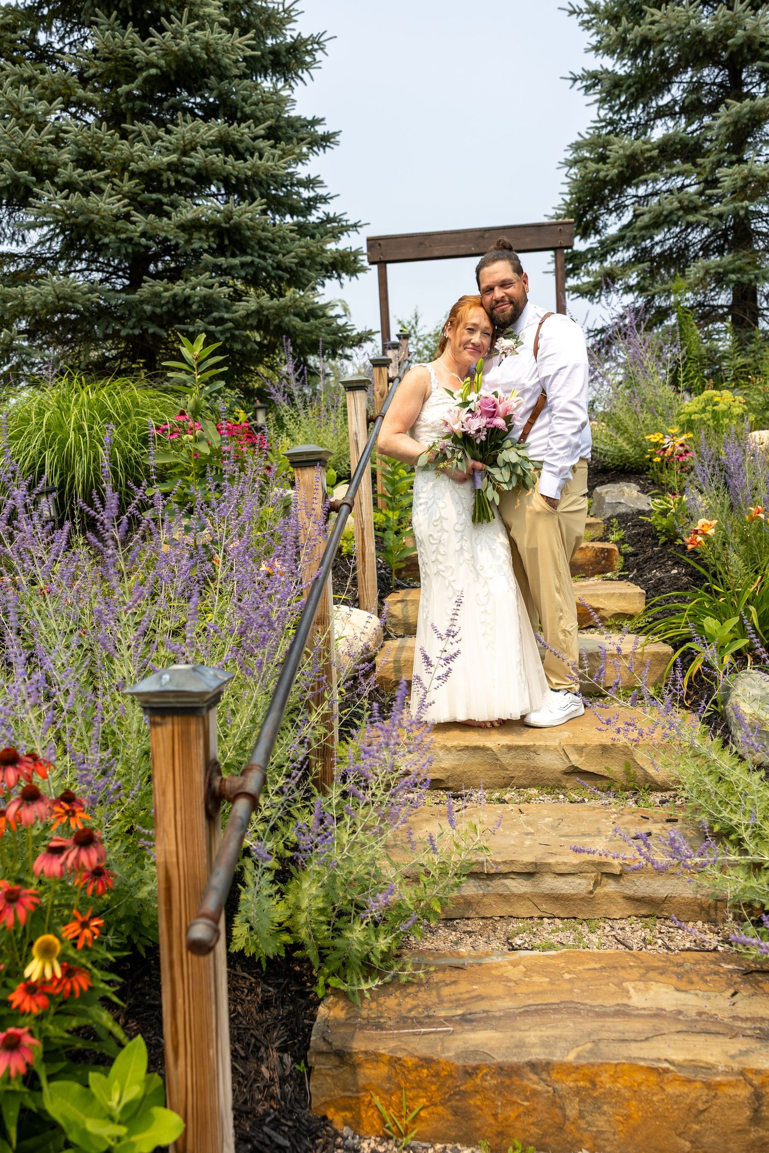 Bride and groom pose on stone garden steps surrounded by lavender and wildflowers on their wedding day.