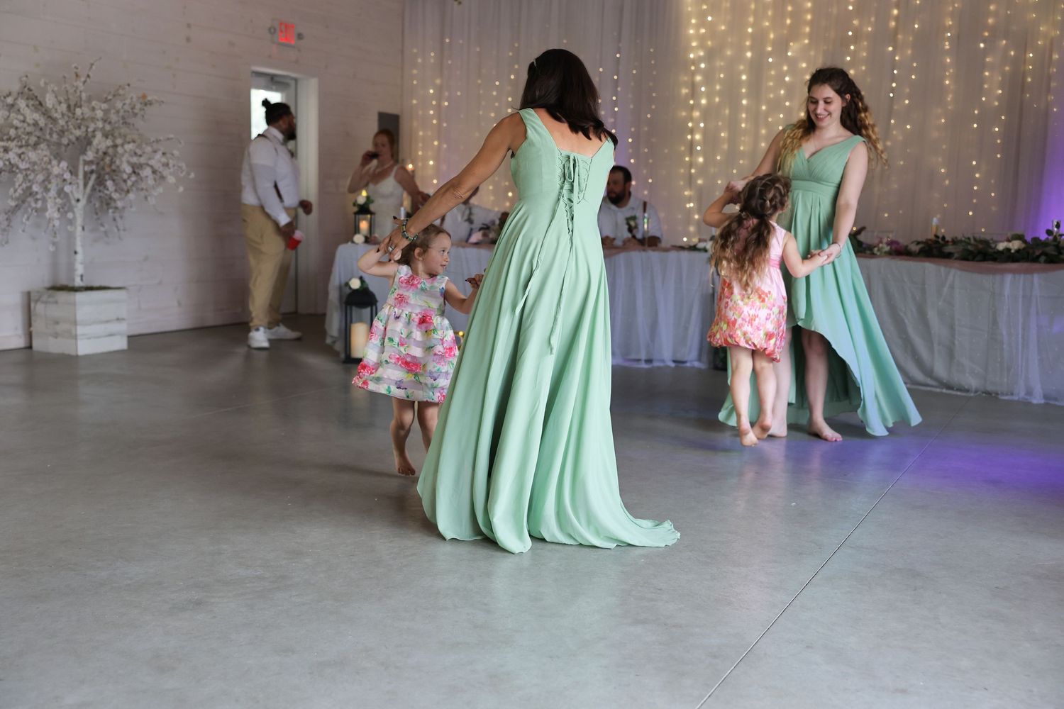 Bridesmaids in mint green gowns dancing with children on a decorated wedding reception dance floor.