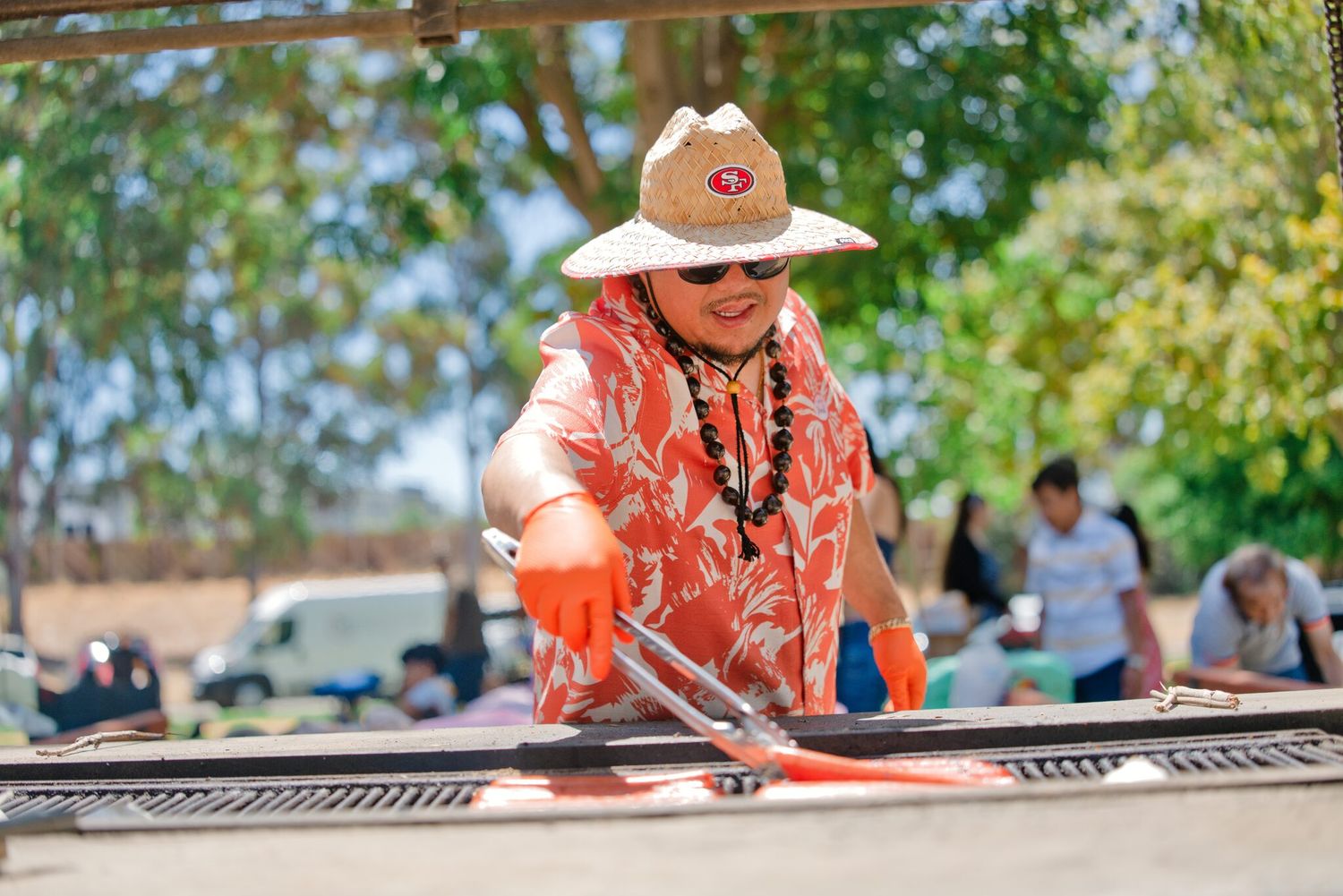 Person in SF 49ers hat and orange gloves working on solar panels outdoors at a sunny community event.