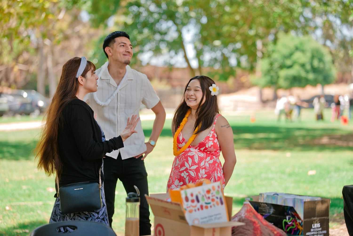 Three friends laughing and socializing outdoors in a sunny park during a casual daytime gathering.
