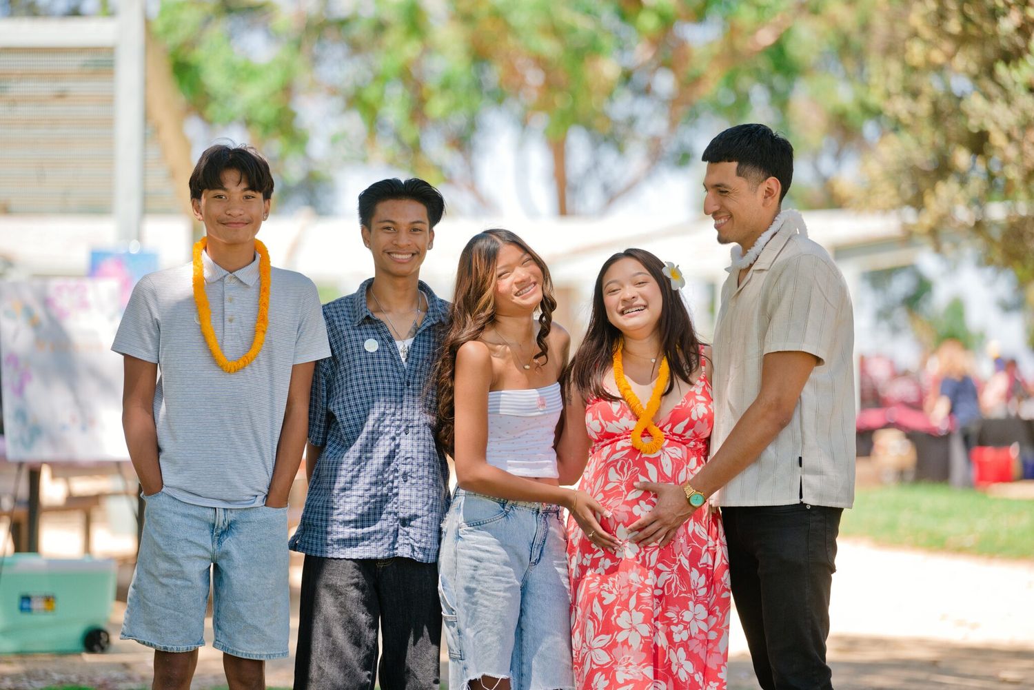 Group of five smiling young adults walking together outdoors at sunny campus event.