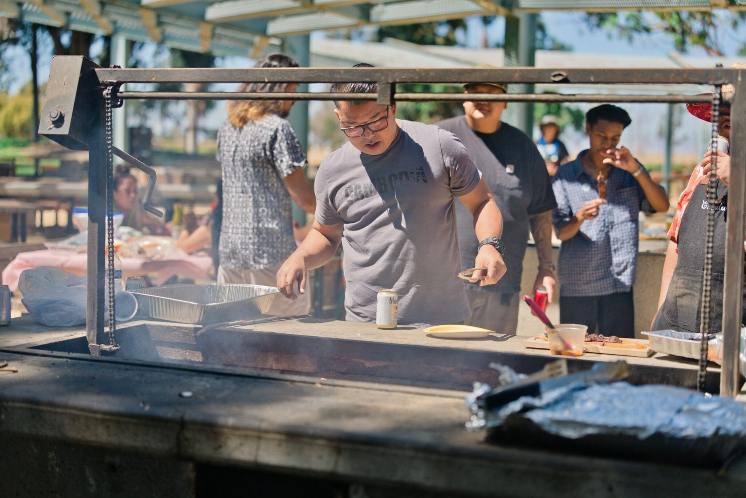 Man grilling food outdoors at a barbecue event with smoke rising from the grill.