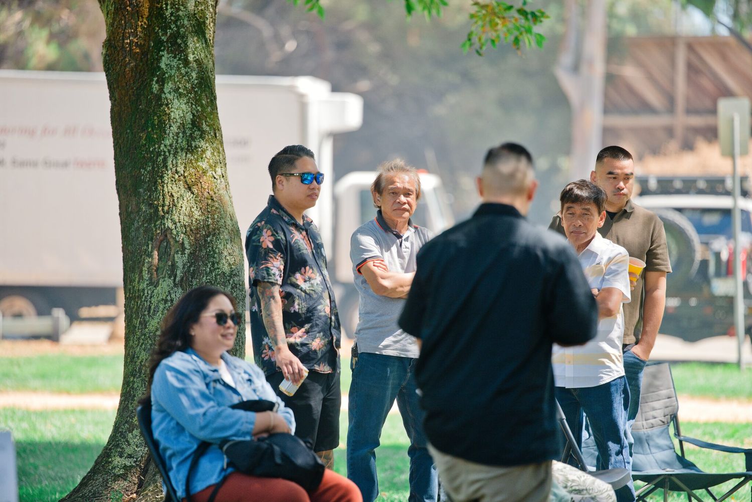 Group of people socializing under a tree in a sunny park on a warm day.