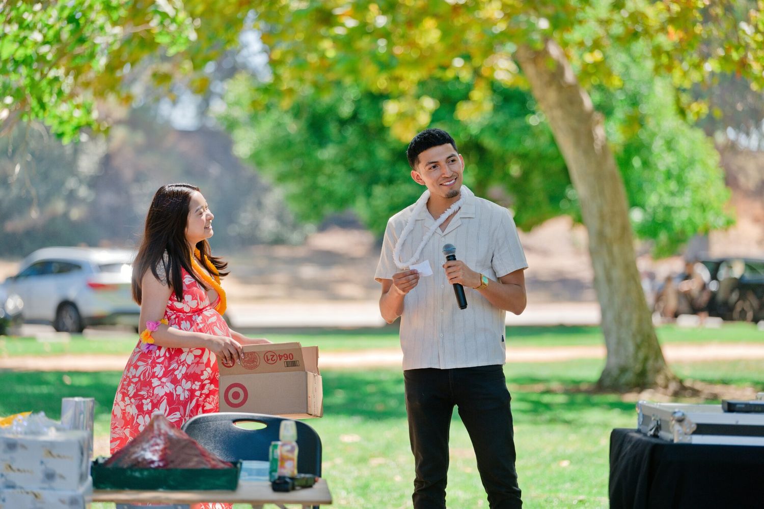 Young man holding a microphone speaks to a woman at a sunny outdoor park gathering.