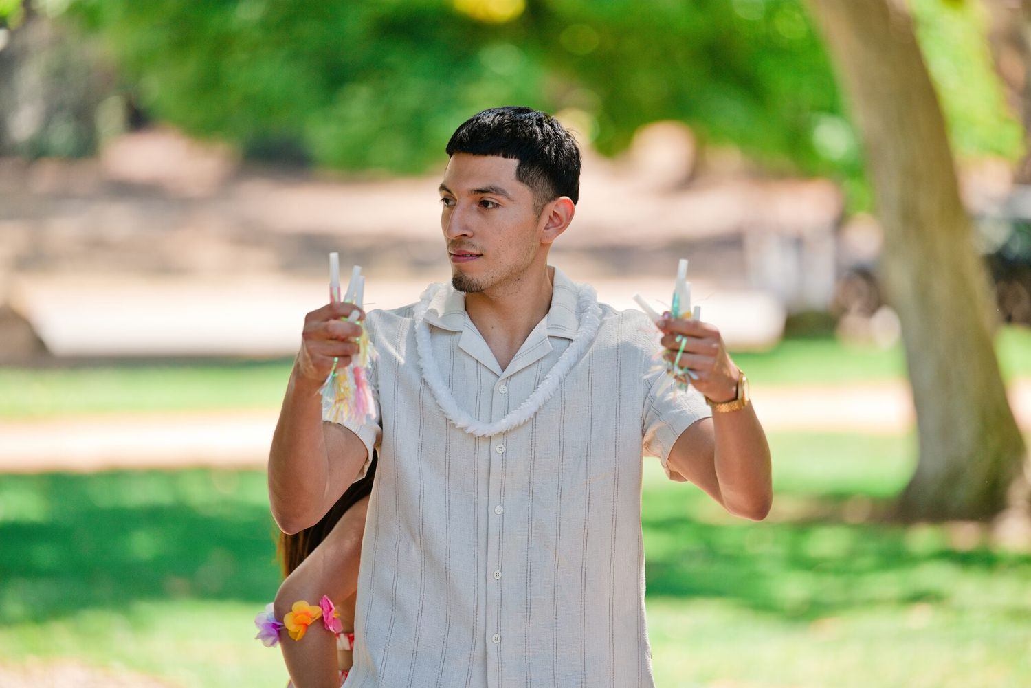 Young man holding two water bottles in a sunny green park setting.