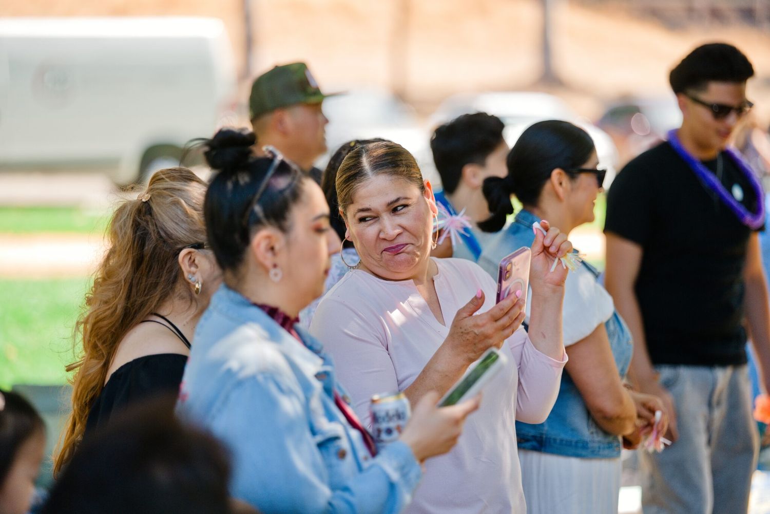 Group of women socializing outdoors at a sunny park gathering, one holding a pink smartphone.