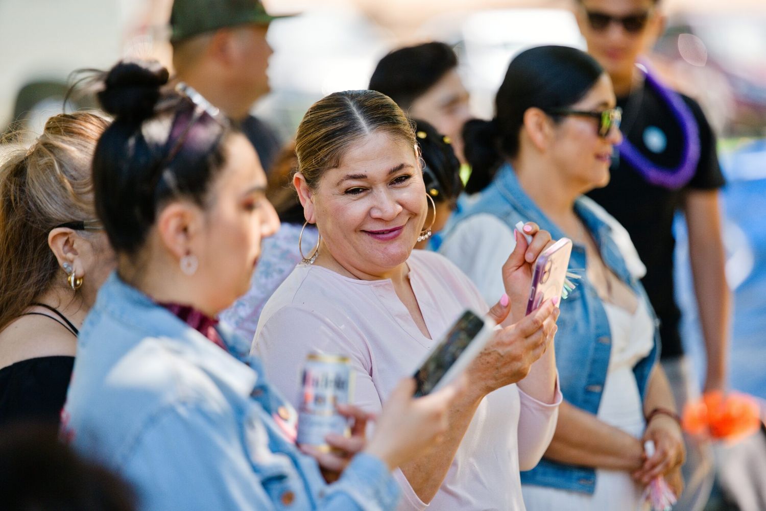 Women smiling and taking photos at an outdoor event on a sunny day.