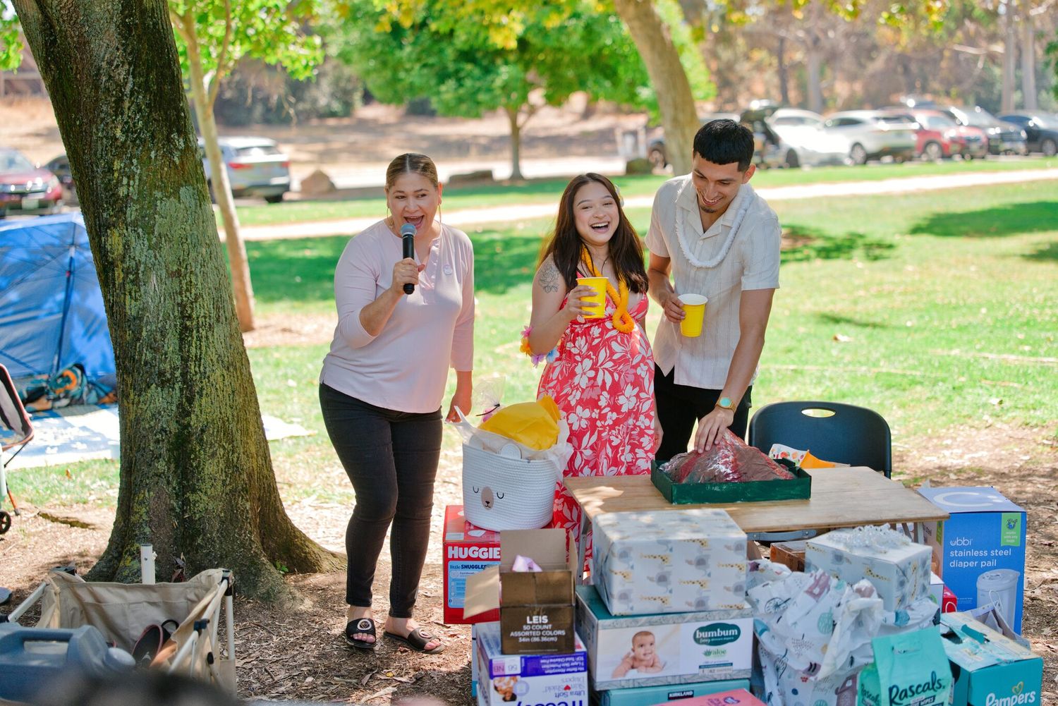Three people stand at a table outdoors surrounded by donated goods at a community park event.