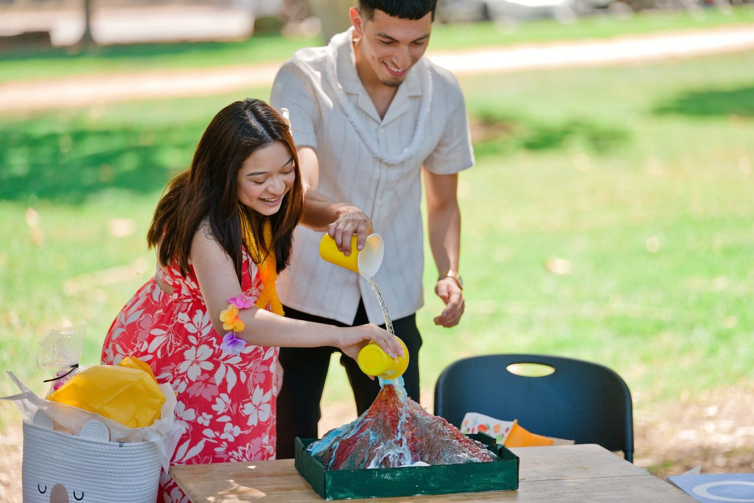 Young couple arranging colorful items in a tray at an outdoor picnic table.