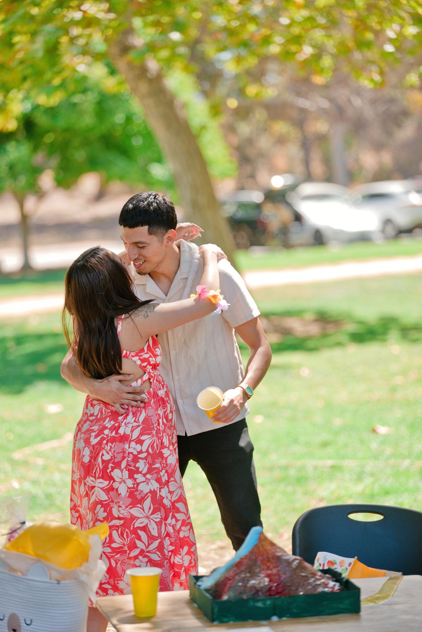 Couple sharing a warm hug at outdoor baby shower celebration with gifts and decorations on table.