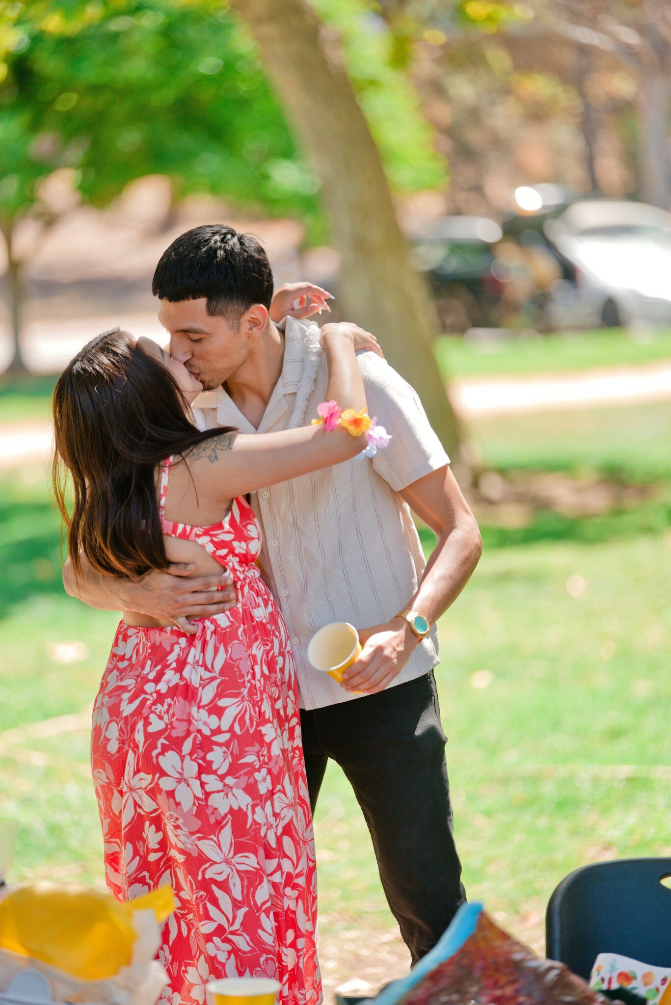 Couple sharing a kiss at an outdoor picnic gathering in a lush green park.