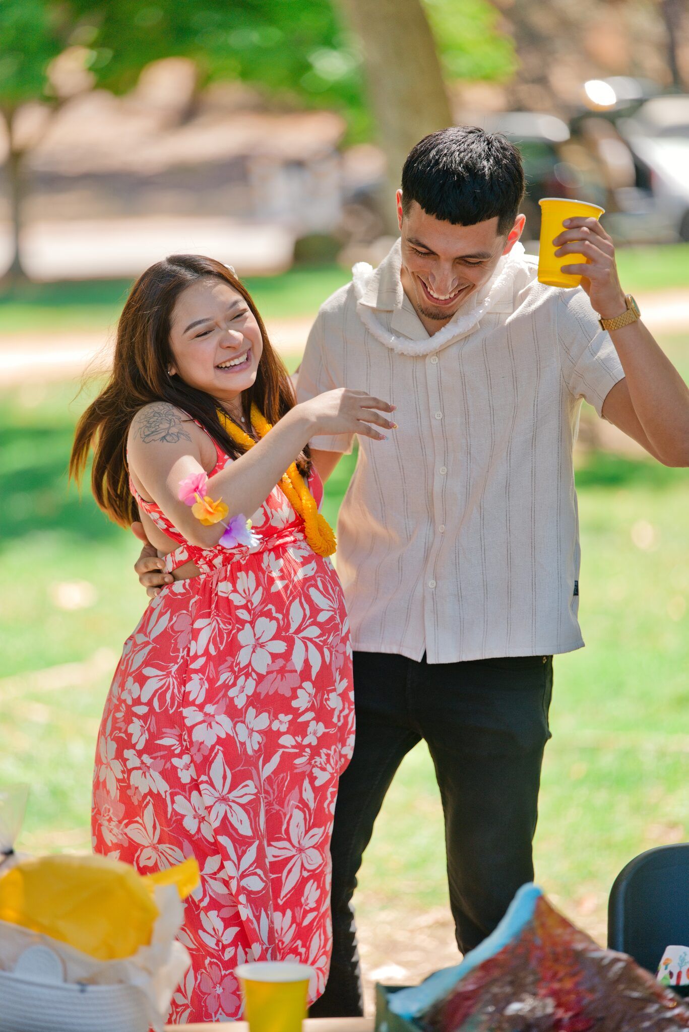 Happy young couple laughing and dancing together at an outdoor park picnic on a sunny day.