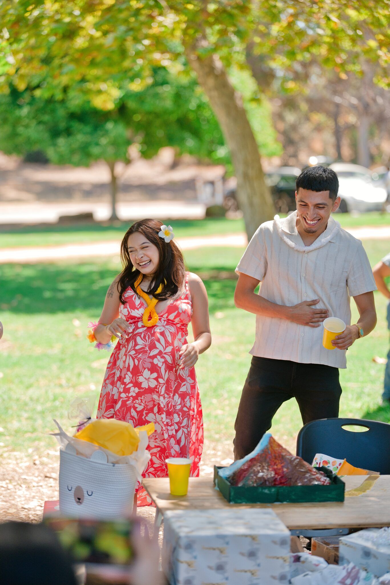 Happy couple laughing at a sunny outdoor park gathering with food on table.