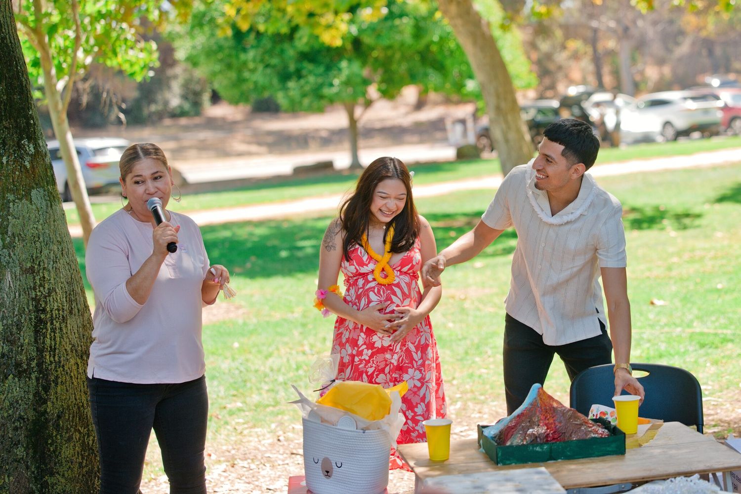 Three friends enjoying an outdoor park picnic together on a sunny day near a wooden table.