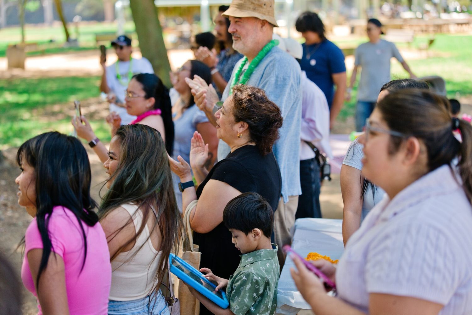 Diverse group of people gathered outdoors under trees at a community park event.
