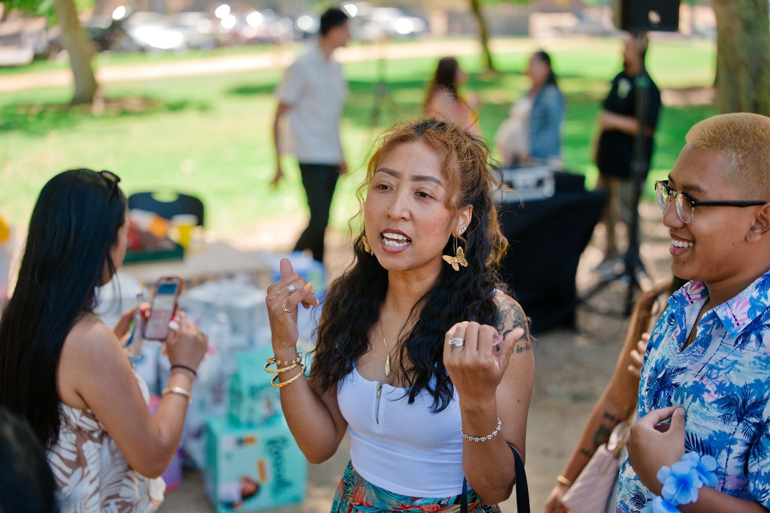Young woman dances joyfully with friends at casual outdoor park gathering on sunny day.