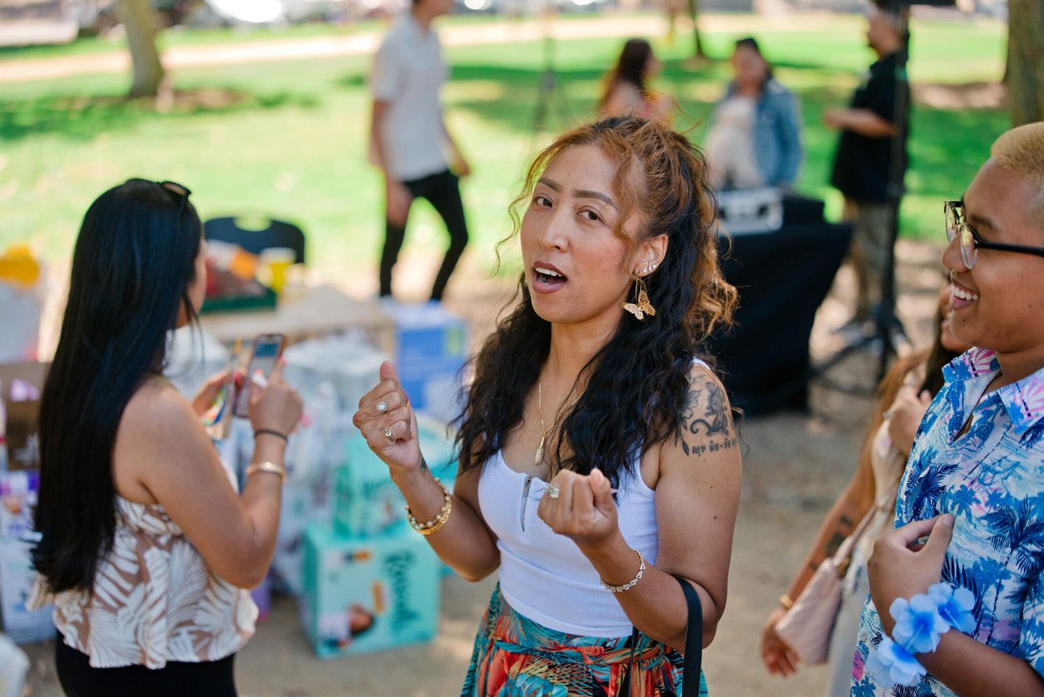 Young woman with tattoos dancing outdoors at a casual gathering, wearing a white top and colorful skirt.