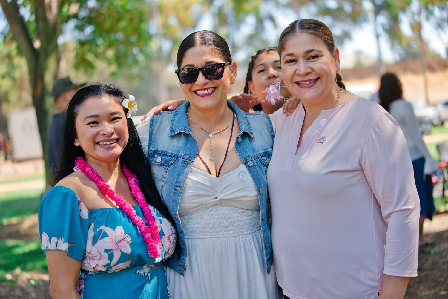 Four women smiling together outdoors at a sunny park community gathering.