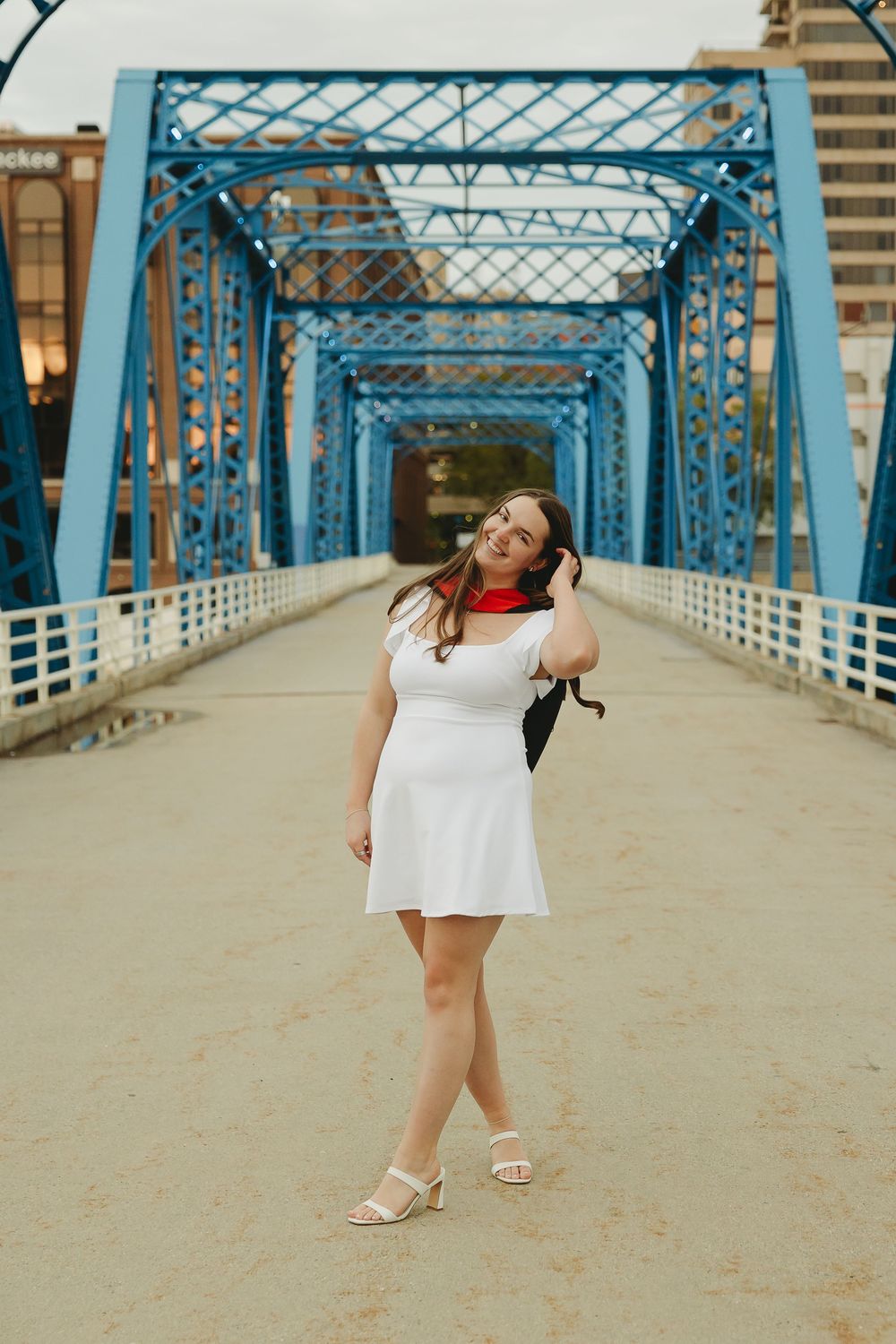Woman in white dress and red scarf poses on blue steel bridge walkway in urban setting.
