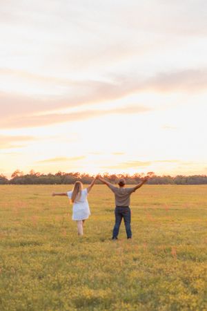 Joyful couple raising their arms in celebration in a sunlit meadow during a beautiful golden sunset.