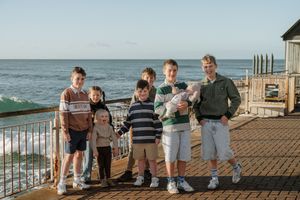 Family group photo with children and adults posing on a seaside deck with ocean waves in the background.
