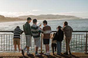 Family group standing at a railing overlooking a scenic coastal bay with misty hills at sunset.