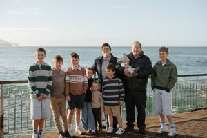 Large family group photo on a seaside pier with ocean views, including children and grandparents posing together.