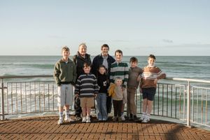 Family group of adults and children posing on a coastal boardwalk with ocean waves in the background.