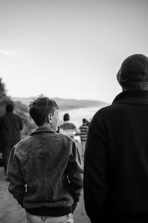 Black and white photo of a boy and man walking toward a coastal vista with other people in the background.