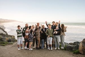 Large family group photo on coastal cliffside with ocean waves and rocky shoreline in background.