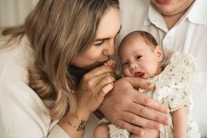 A mother kisses her newborn baby's hand while the father holds the infant in a tender family portrait.