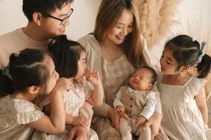 Asian family with parents and four children, including a newborn baby, sharing a warm moment together indoors.