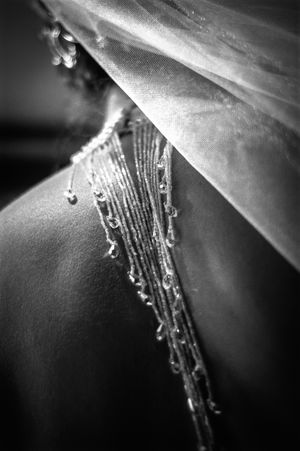 Close-up black and white detail of a wedding dress back with delicate beaded straps and sheer veil.