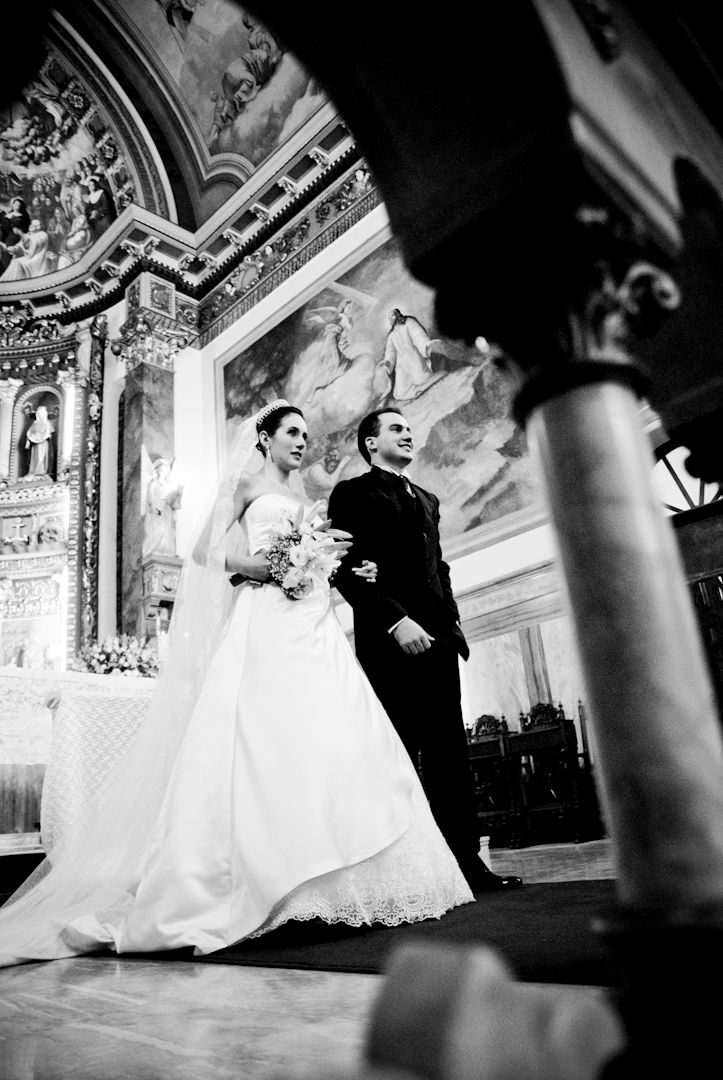 Bride and groom stand together during wedding ceremony inside an ornate church with frescoed ceilings.