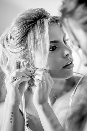 Black and white photo of a bride having her earring put on while getting ready for her wedding day.