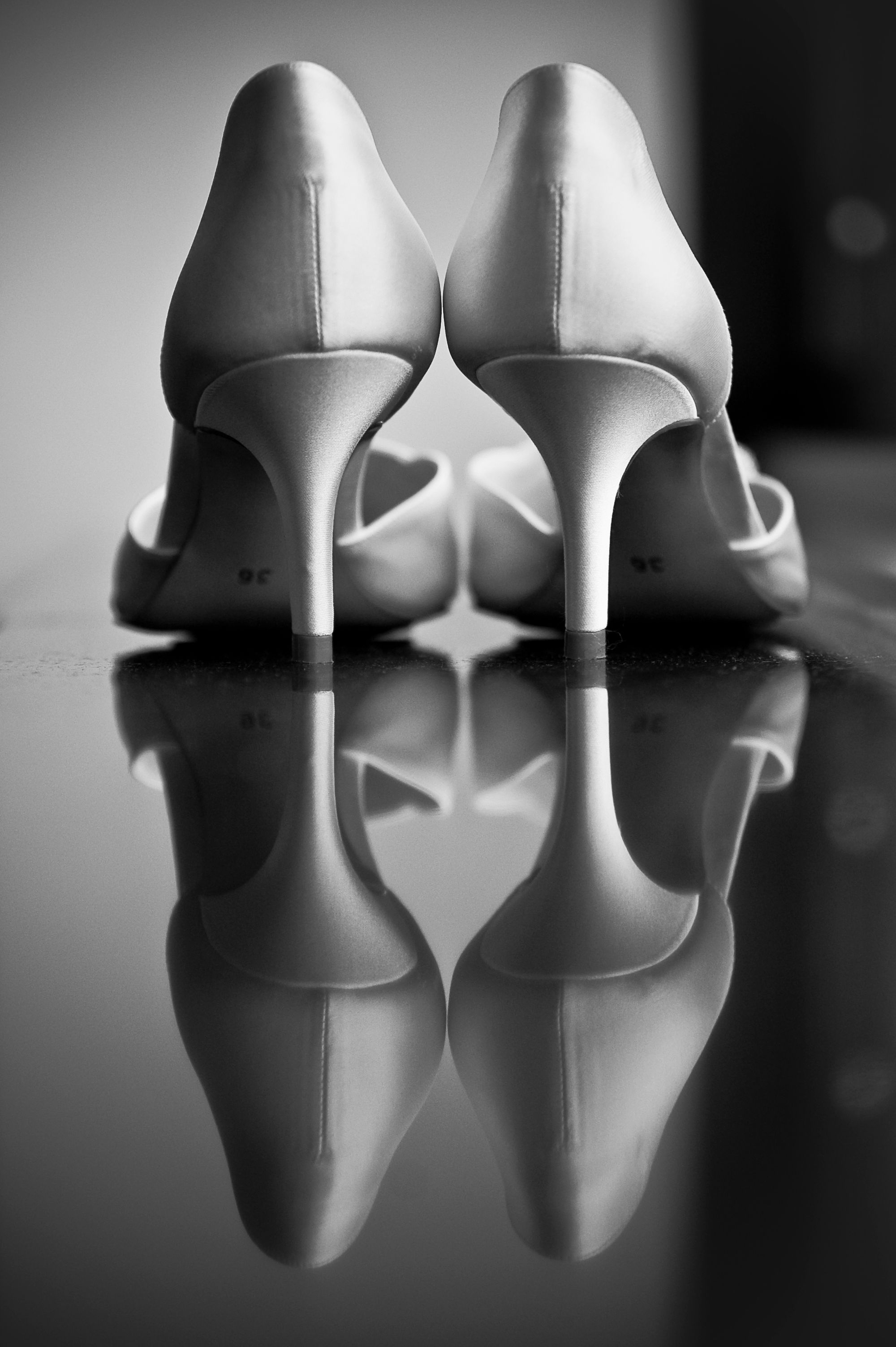 Black and white artistic photo of elegant white bridal heels reflected on a glossy surface.