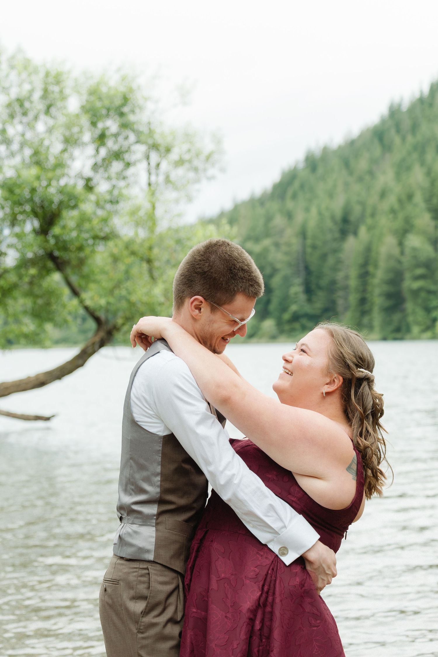Couple in wedding attire laughing and falling in snow while snowshoeing in a winter mountain landscape.