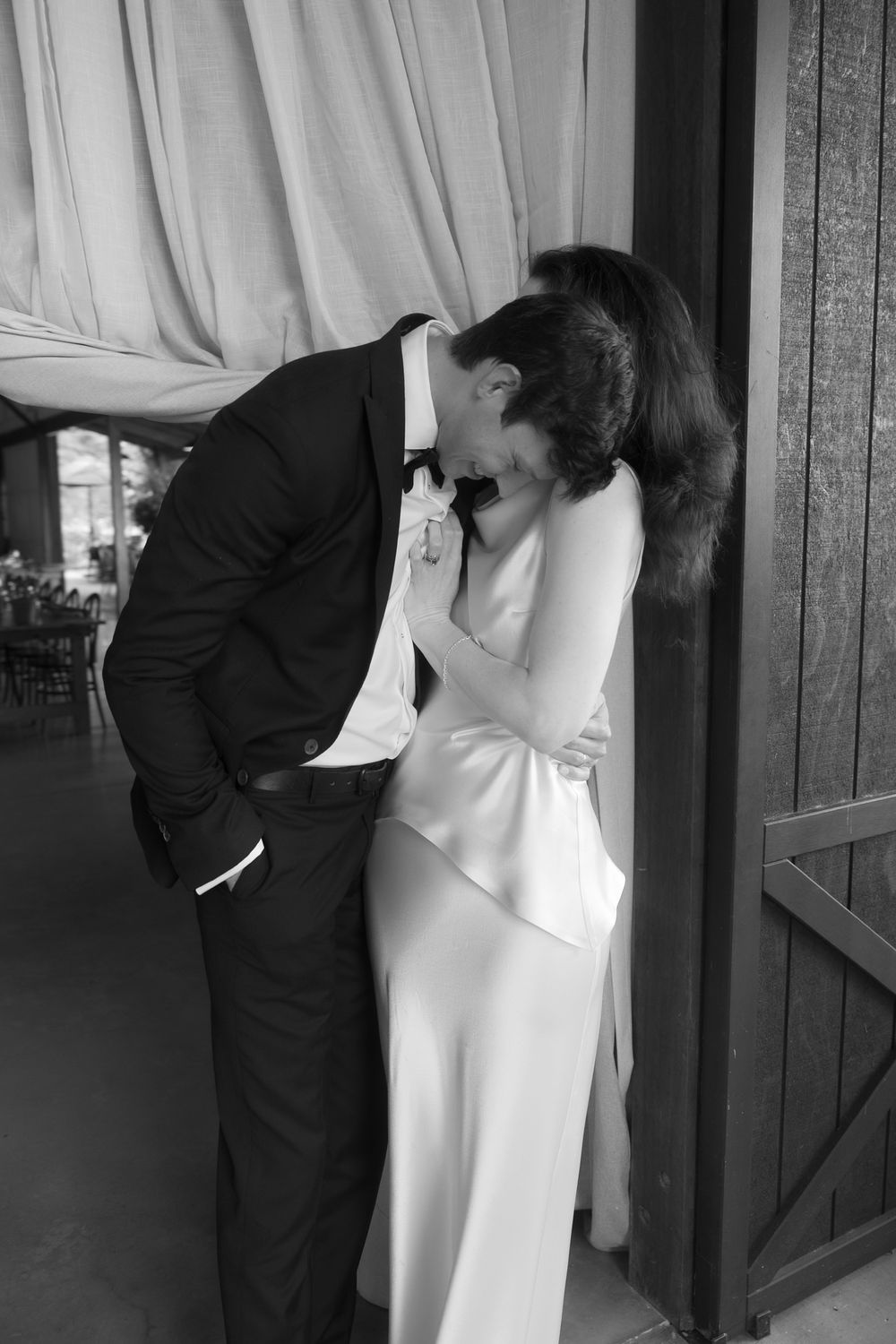 Black and white photo of a couple sharing a romantic kiss, groom in suit and bride in elegant white gown.