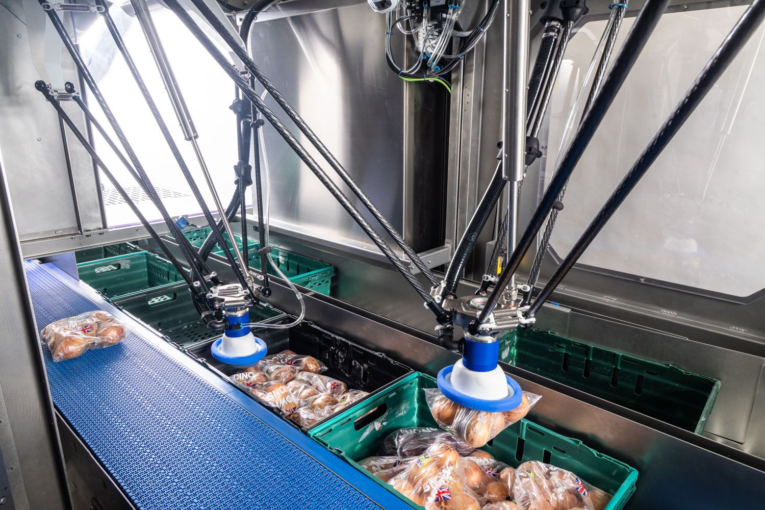 Delta robots sorting packaged food products into green trays on an automated conveyor line in a food processing facility.