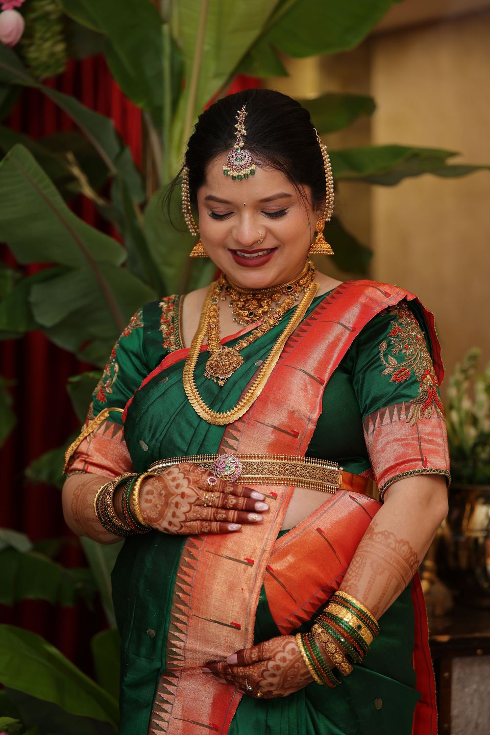 South Indian bride in green and red silk saree with gold jewelry and mehndi hands.