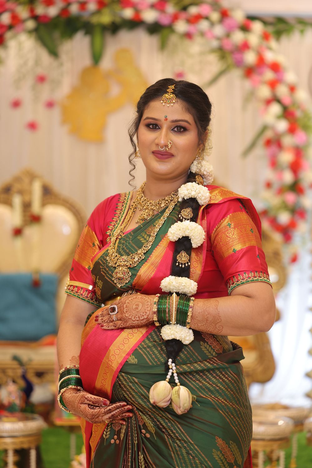 Indian bride in green pink silk saree with floral garland and gold bridal jewelry.